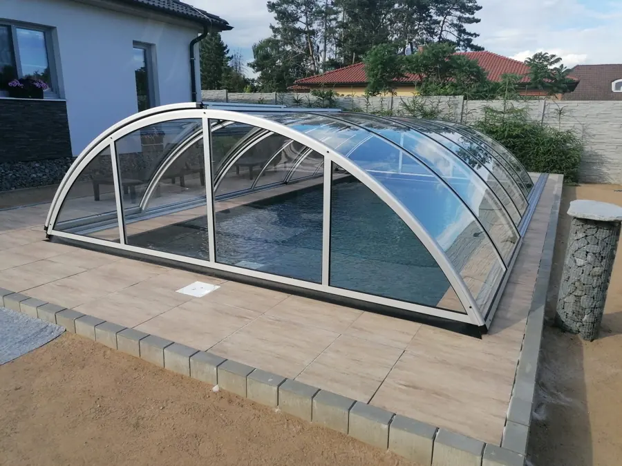 Gewölbte Poolüberdachung mit Aluminiumprofilen und transparenten Elementen neben einem Wohnhaus