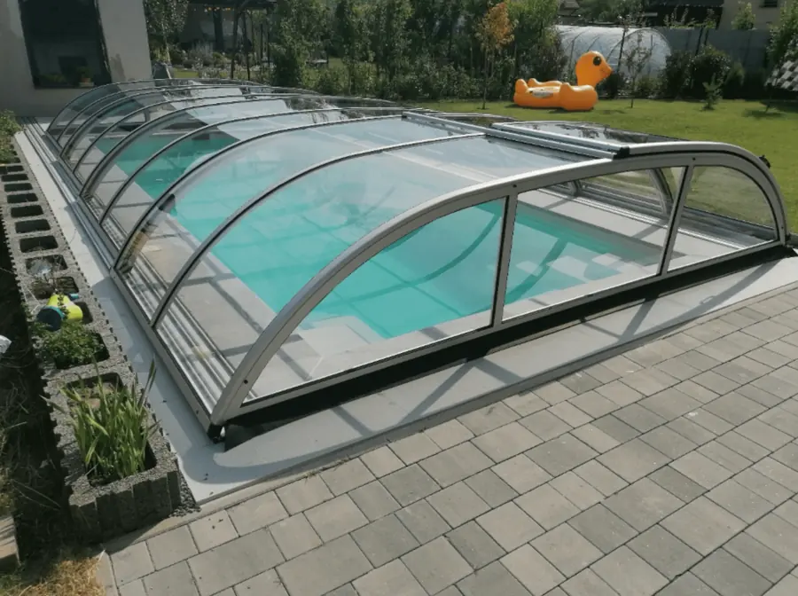 Teleskopierbare Poolüberdachung, teilweise geöffnet, über einem Pool mit türkisem Wasser